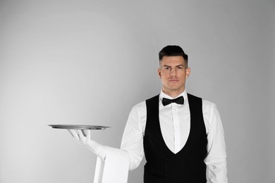 Photo of Handsome butler with tray on light grey background