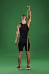 Photo of Athletic woman exercising with elastic resistance band on green background, back view