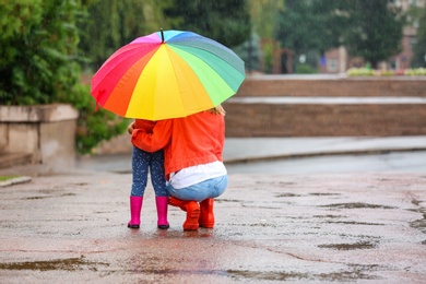 Mother and daughter with bright umbrella under rain outdoors