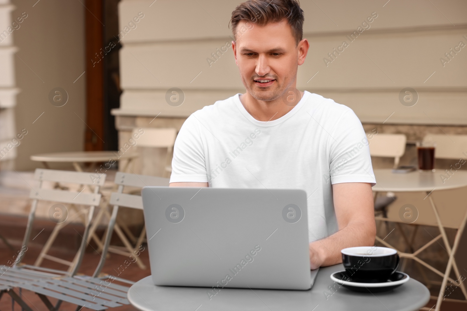 Photo of Handsome man working on laptop at table in outdoor cafe