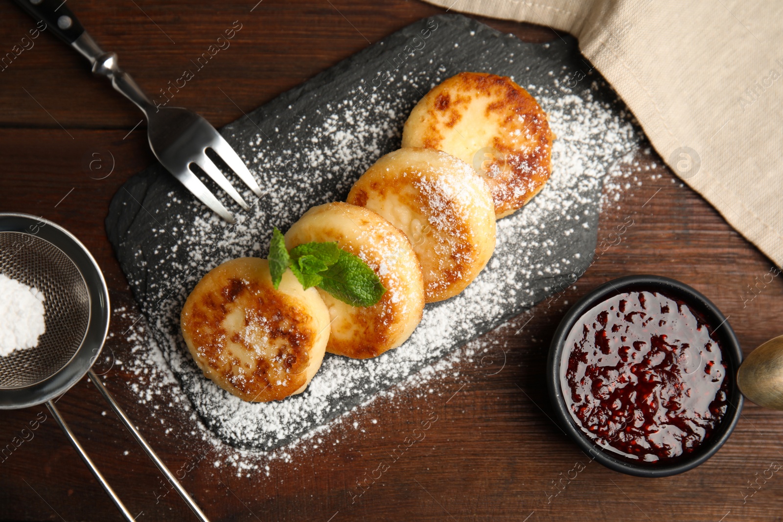 Photo of Delicious cottage cheese pancakes with icing sugar and jam on wooden table, flat lay