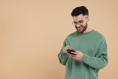 Happy young man using smartphone on beige background, space for text