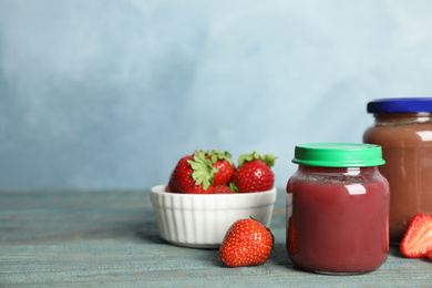 Jars with baby food and fresh strawberries on wooden table against light blue background, space for text