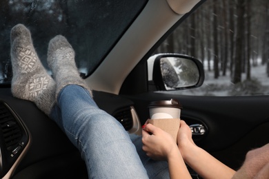 Photo of Young woman in warm socks with coffee resting inside car, closeup