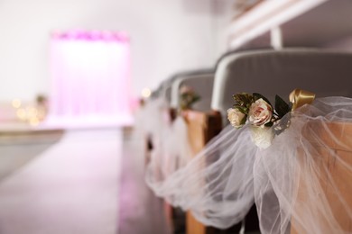 Photo of Chairs decorated with flowers and tulle indoors, closeup. Wedding ceremony