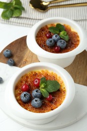 Photo of Delicious creme brulee with berries and mint in bowls on white table, closeup