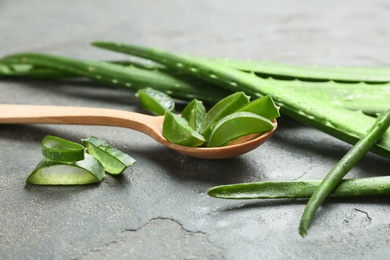 Photo of Wooden spoon and fresh aloe vera leaves on gray table