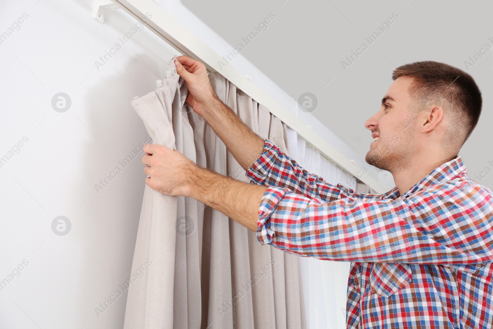 Photo of Man hanging window curtain indoors. Interior decor element
