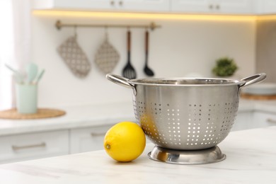 Photo of Empty colander and fresh lemon on white marble table in kitchen. Space for text