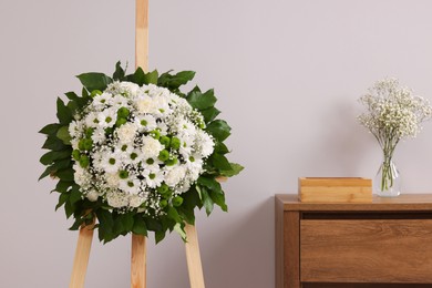 Photo of Funeral wreath of flowers on wooden stand near grey wall in room