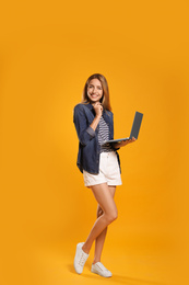Full length portrait of young woman with modern laptop on yellow background