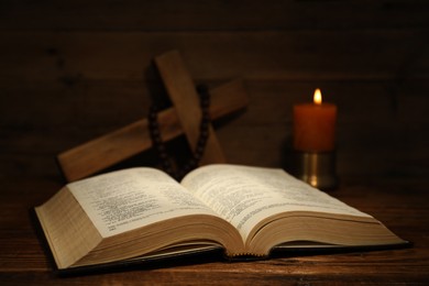 Photo of Bible, cross, rosary beads and church candle on wooden table