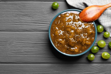 Photo of Delicious gooseberry jam, spoon and fresh berries on grey wooden table, flat lay. Space for text