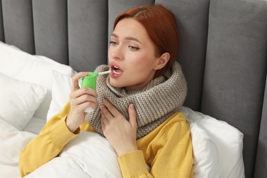 Photo of Young woman with scarf using throat spray in bed