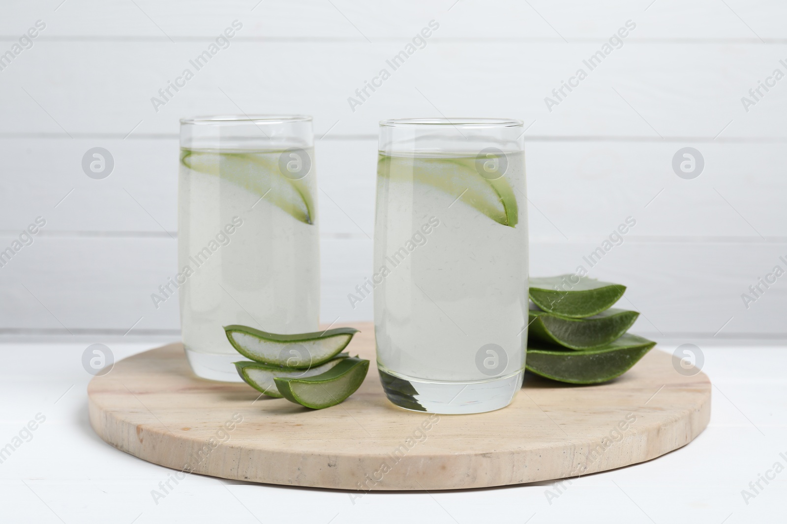 Photo of Tasty aloe juice in glasses and cut fresh leaves on white table