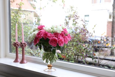 Vase with beautiful bouquet of roses and candles on windowsill indoors, space for text