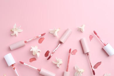 Different lip glosses, applicators and flowers on pink background, flat lay. Space for text