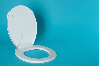 Photo of New plastic toilet seat on light blue background, space for text