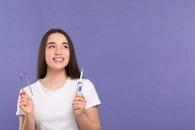 Photo of Happy woman with tongue cleaner and electric toothbrush on violet background, space for text