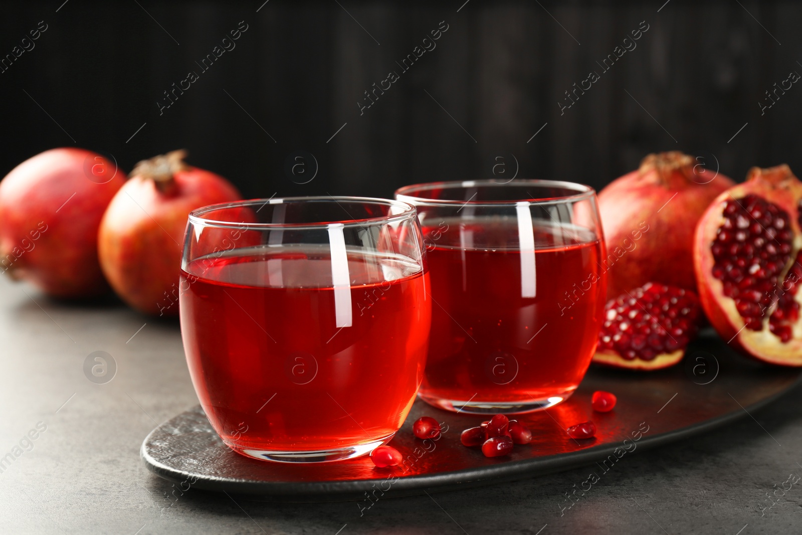 Photo of Tasty pomegranate juice in glasses and fresh fruits on grey table