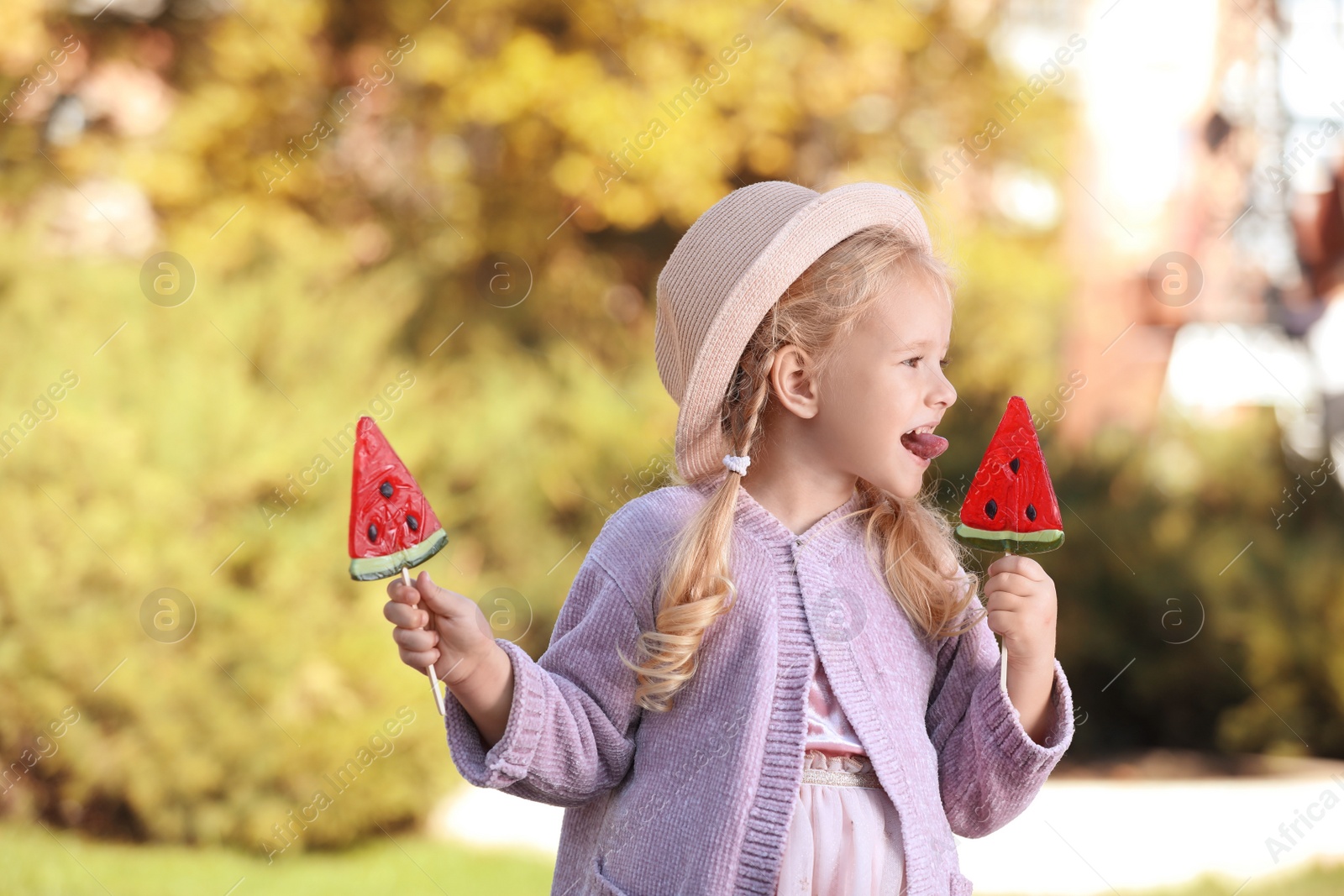 Photo of Cute little girl with tasty candies outdoors