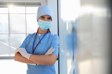 Doctor in medical gloves, protective mask and scrubs indoors. Space for text