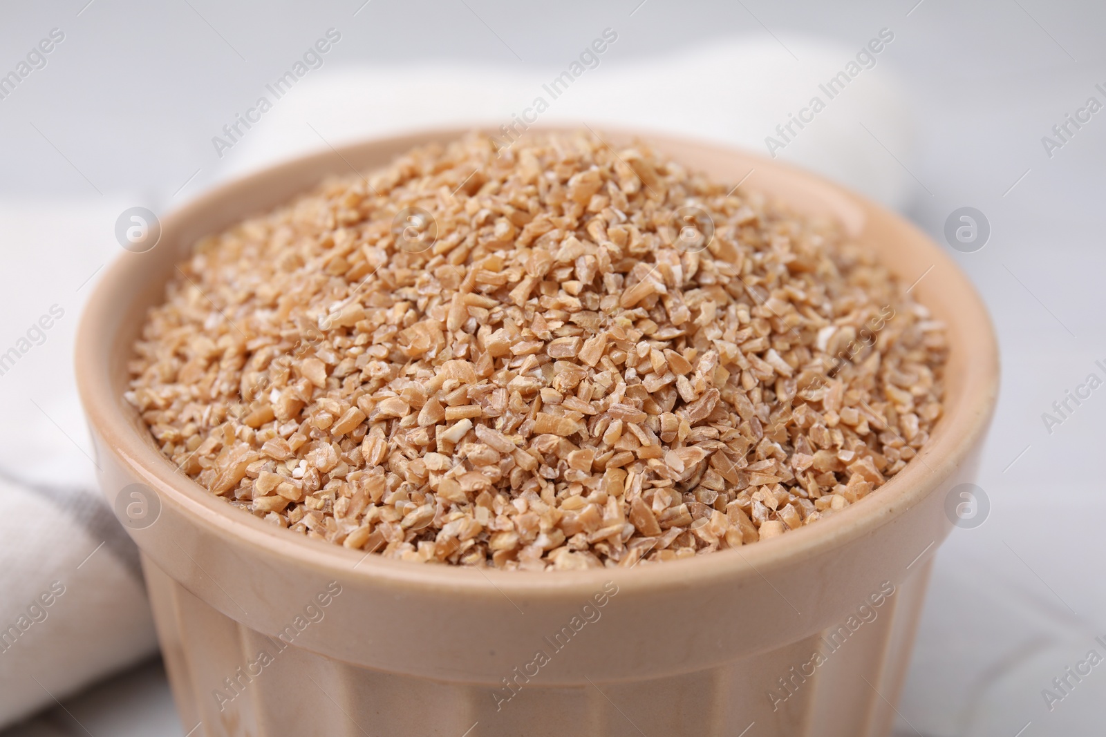 Photo of Dry wheat groats in bowl on light table, closeup