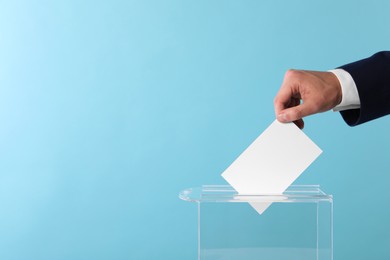 Man putting his vote into ballot box on light blue background, closeup. Space for text