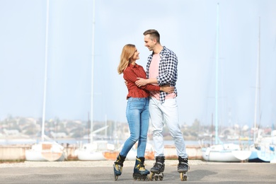 Happy lovely couple roller skating on embankment. Space for text