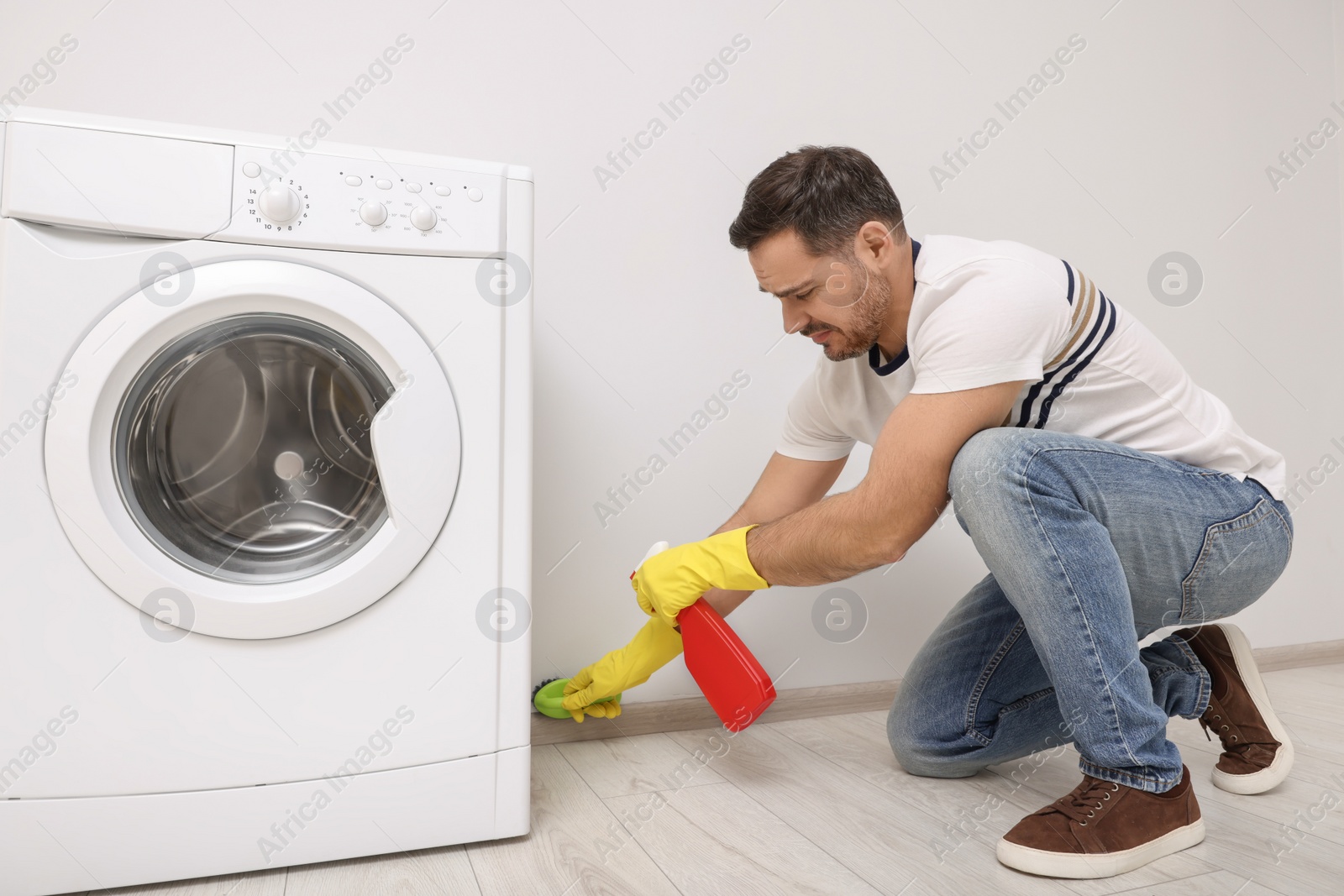 Photo of Man in rubber gloves cleaning wall with sprayer and brush indoors