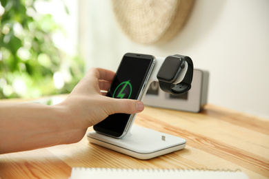 Man putting mobile phone onto wireless charger at wooden table, closeup. Modern workplace accessory