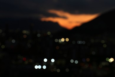 Photo of Blurred view of sunset with dark clouds above big mountains and night city