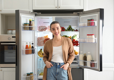 Photo of Happy young woman near open refrigerator in kitchen