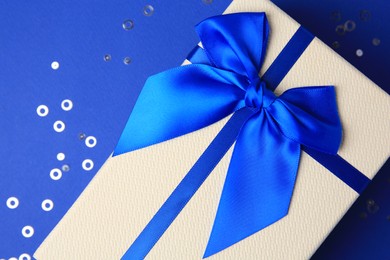 Photo of Beautiful gift box with bow and confetti on blue background, top view