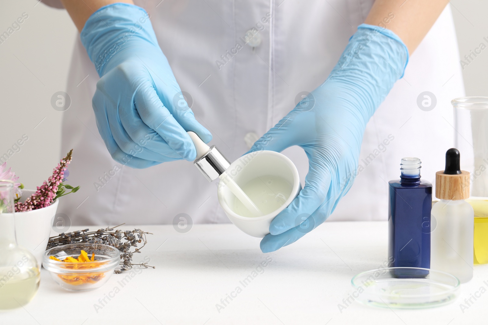 Photo of Scientist developing cosmetic oil at white table, closeup