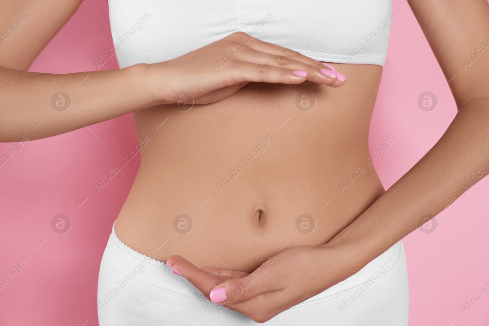 Photo of Woman in underwear holding something near her belly on pink background, closeup. Healthy stomach