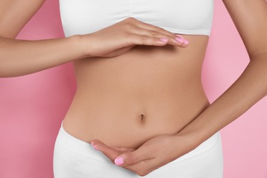 Woman in underwear holding something near her belly on pink background, closeup. Healthy stomach