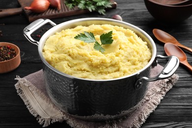 Photo of Pot of tasty mashed potatoes with parsley on black wooden table