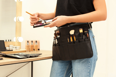 Photo of Professional makeup artist with eyeshadow palette and belt organizer full of tools in studio, closeup