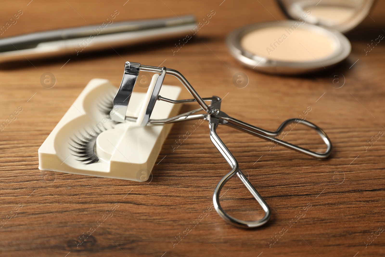 Photo of False eyelashes and curler on wooden table, closeup
