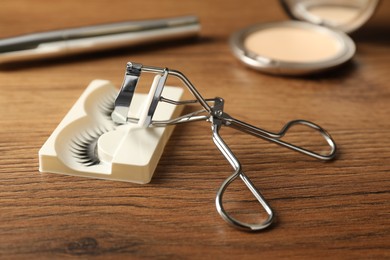 Photo of False eyelashes and curler on wooden table, closeup