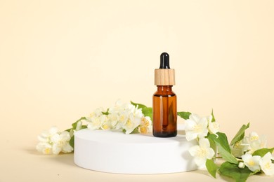 Photo of Presentation of essential oil in bottle and beautiful jasmine flowers against beige background, space for text