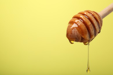 Delicious honey flowing down from dipper against yellow background, closeup. Space for text