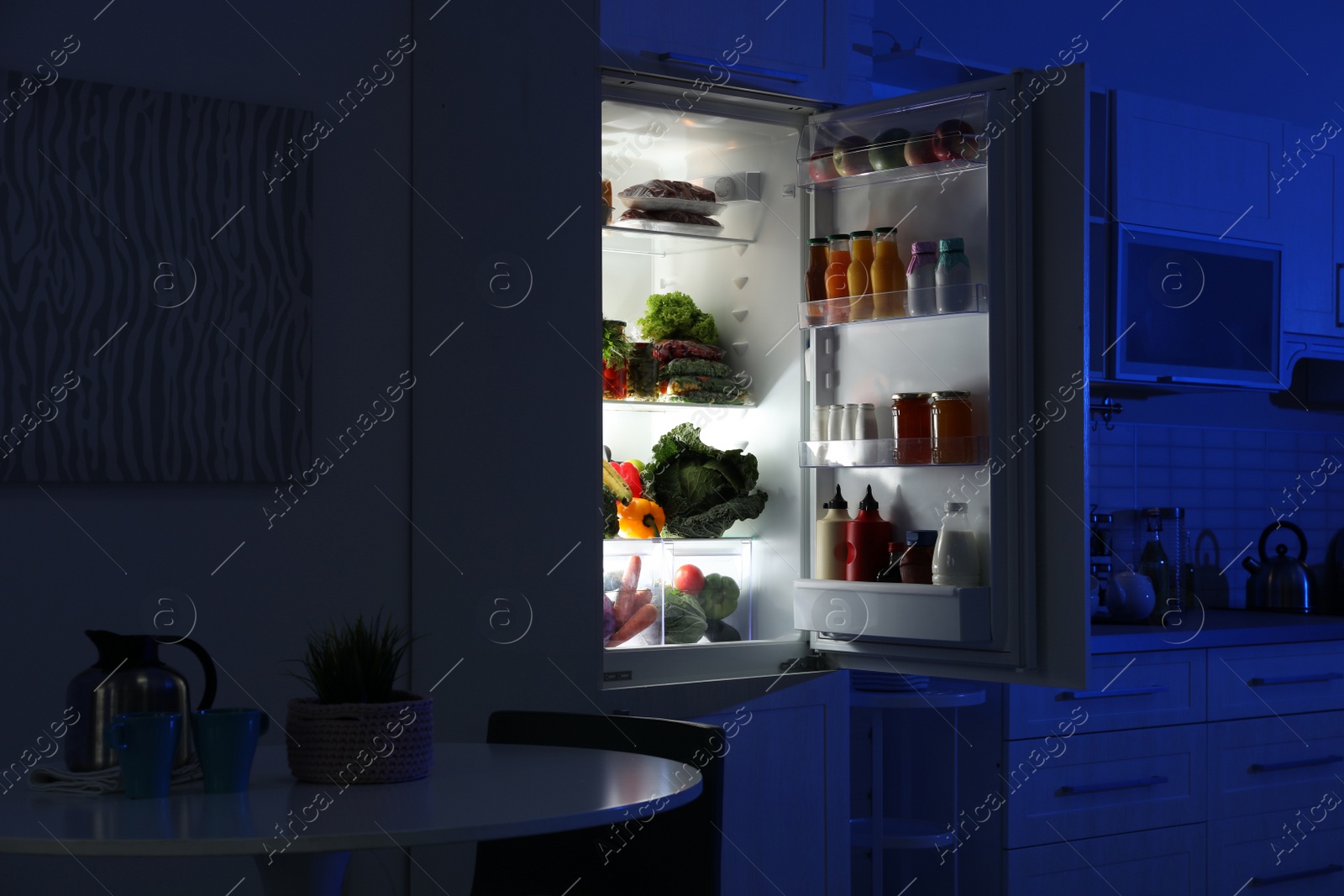 Photo of Open refrigerator full of products in stylish kitchen interior at night