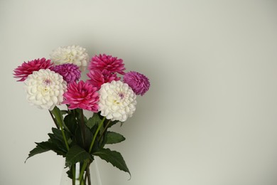 Photo of Bouquet of beautiful Dahlia flowers near white wall, space for text