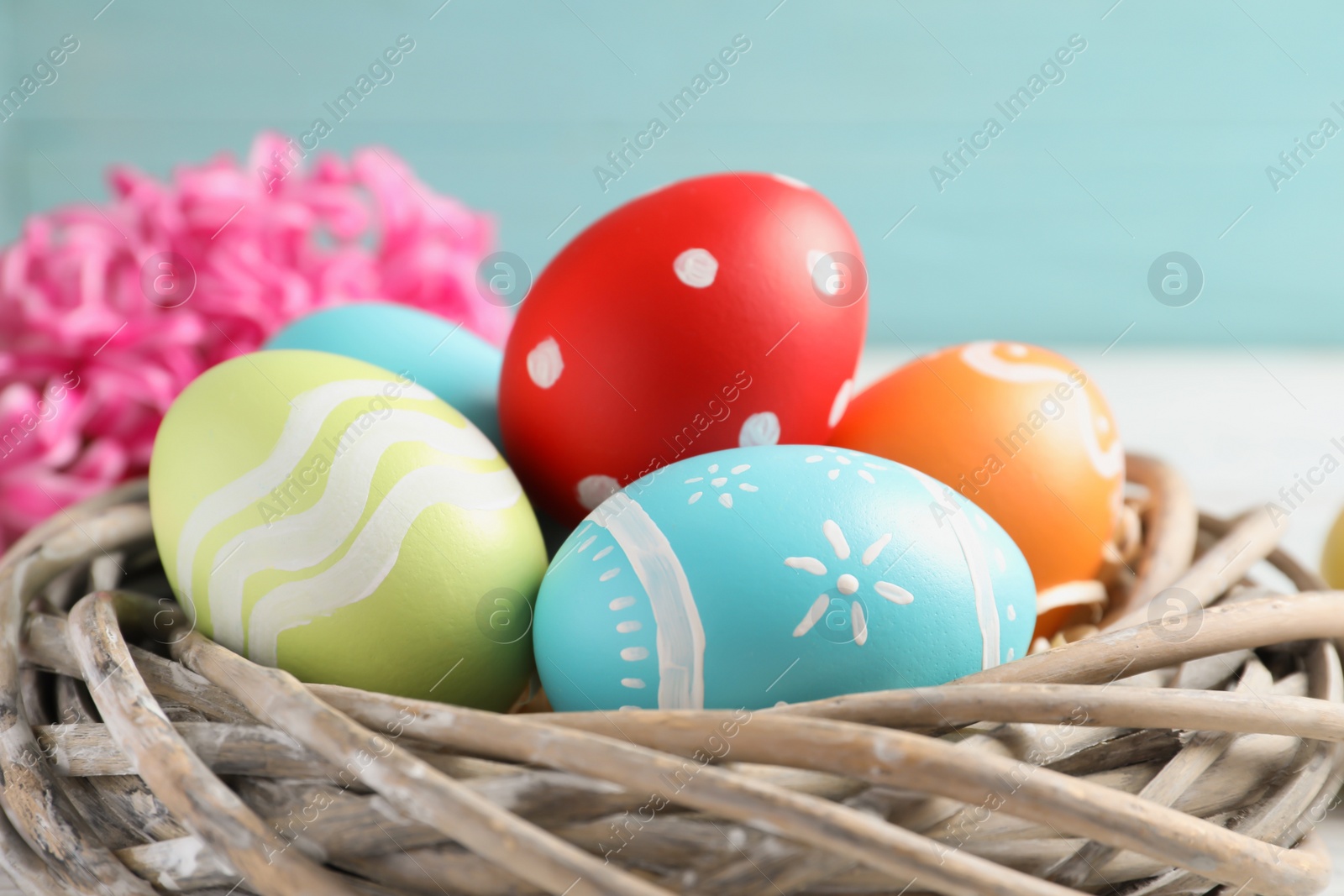 Photo of Colorful painted Easter eggs in wicker nest, closeup
