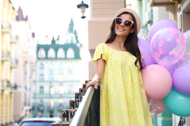 Photo of Beautiful young woman with color balloons on city street