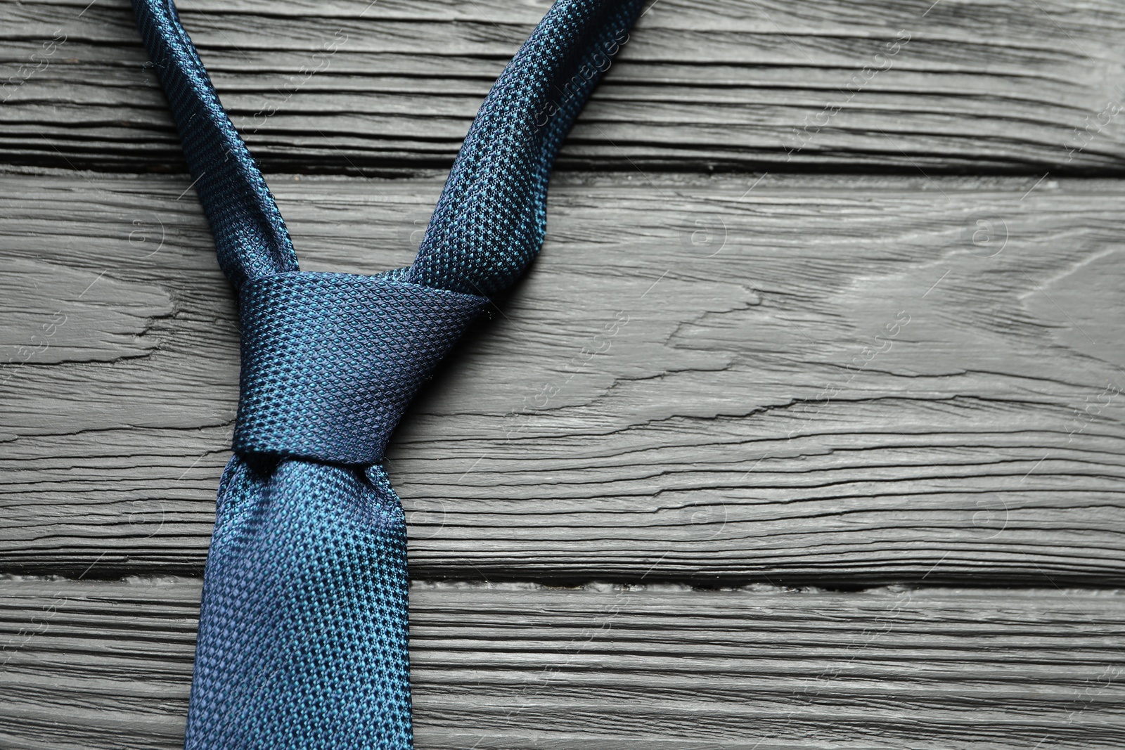 Photo of One blue necktie on black wooden table, top view. Space for text