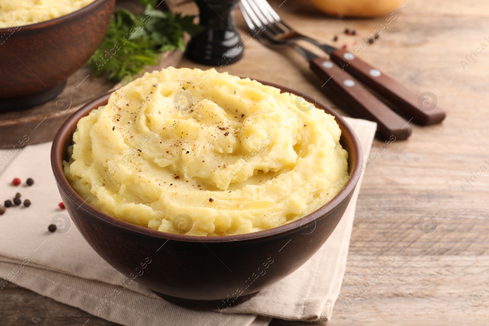 Photo of Bowl of tasty mashed potatoes with black pepper served on wooden table