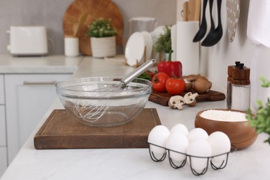 Metal whisk, bowl and different products on white table in kitchen